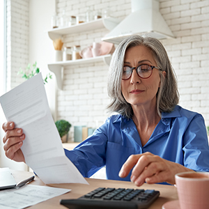 Older woman uses a calculator, reviewing documents for DIY estate planning in New York.