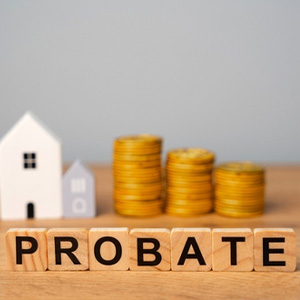 Wooden blocks spelling PROBATE with stacks of coins and miniature houses, representing an estate