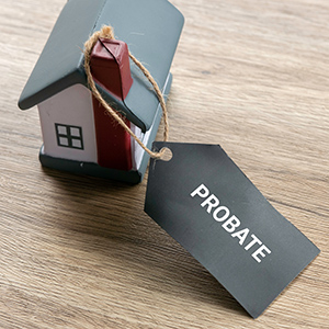 Small house figurine with a tag labeled probate resting on a wooden surface