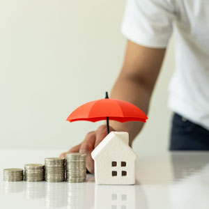 Protecting assets with estate planning: house model, coins, and red umbrella symbolizing security.